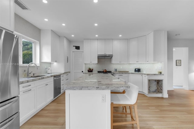 kitchen with under cabinet range hood, a sink, appliances with stainless steel finishes, light wood-type flooring, and a center island