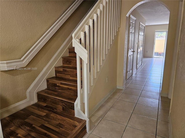 stairway featuring baseboards, arched walkways, a textured ceiling, and tile patterned floors