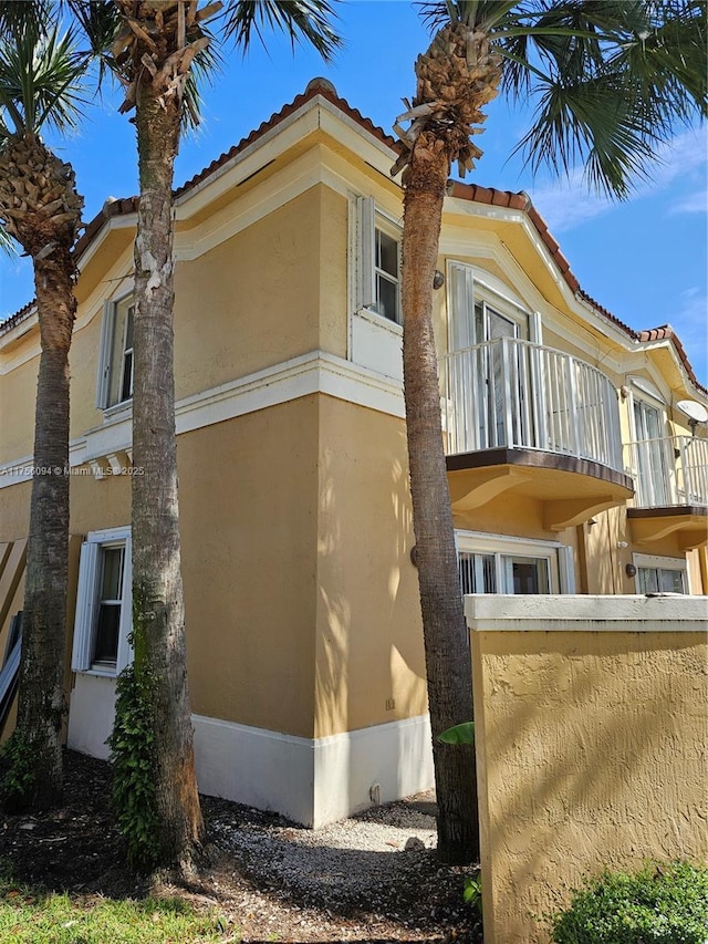 view of property exterior with a tiled roof, a balcony, and stucco siding