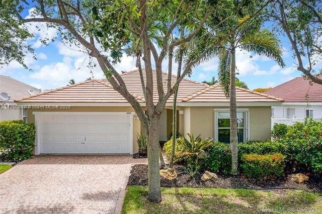 single story home with a garage, a tile roof, decorative driveway, and stucco siding