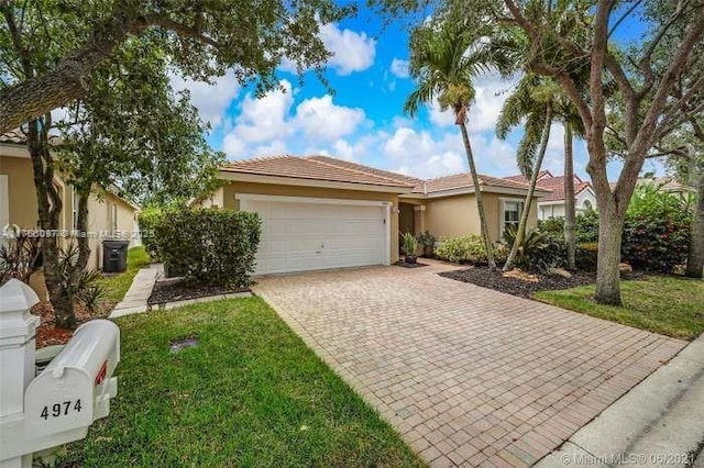 single story home with a garage, decorative driveway, a front yard, and stucco siding