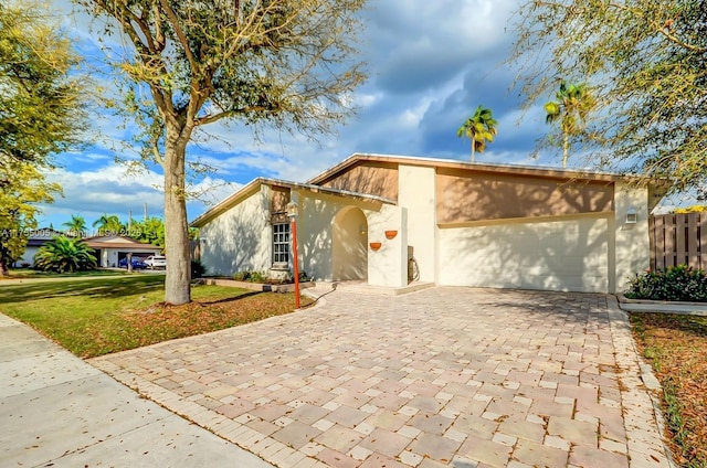 mid-century home with an attached garage, fence, decorative driveway, stucco siding, and a front lawn