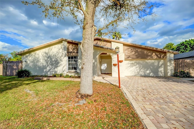 mid-century modern home featuring an attached garage, fence, decorative driveway, stucco siding, and a front yard