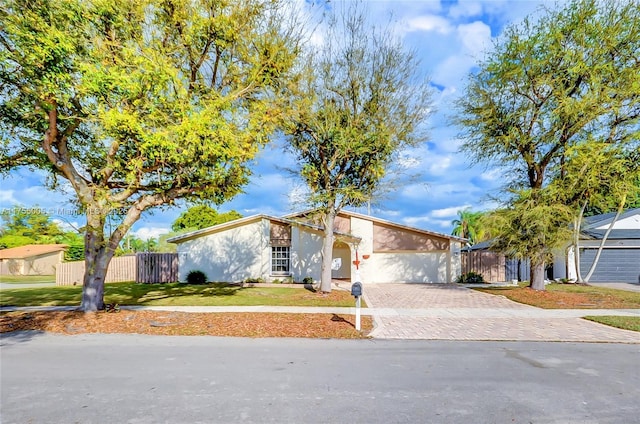 mid-century inspired home with a garage, fence, decorative driveway, stucco siding, and a front lawn