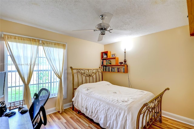 bedroom featuring a textured ceiling, light wood-type flooring, a ceiling fan, and baseboards