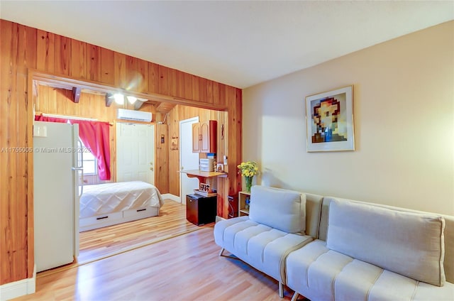 bedroom with light wood finished floors, a wall mounted AC, freestanding refrigerator, and wooden walls