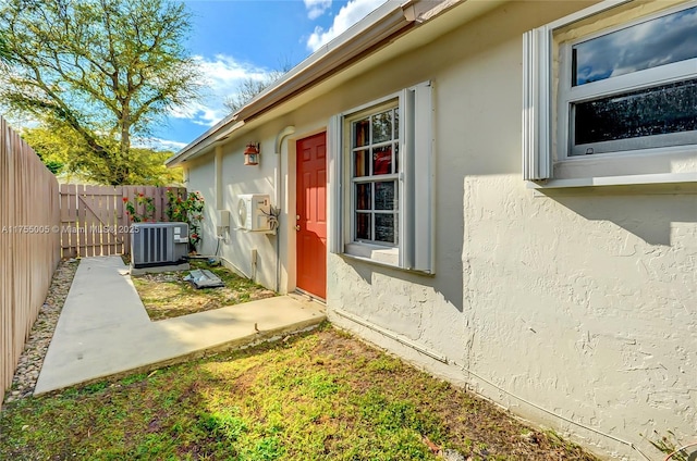 property entrance featuring central air condition unit, fence, and stucco siding