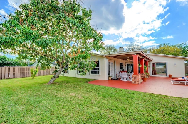 back of property with stucco siding, a lawn, a ceiling fan, a patio area, and fence