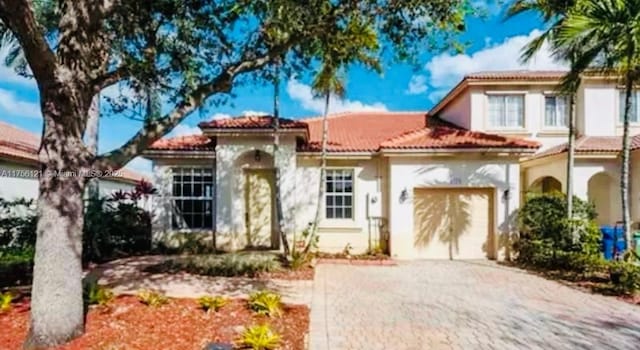 mediterranean / spanish home featuring a tiled roof, decorative driveway, and an attached garage