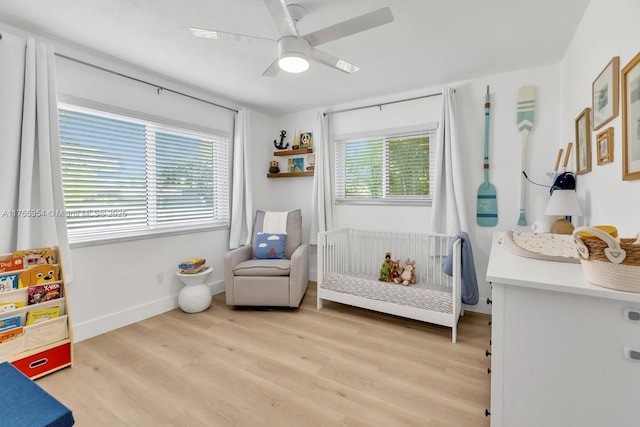 bedroom with a crib, light wood-style floors, multiple windows, and baseboards