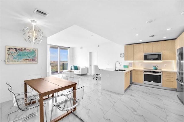 kitchen featuring appliances with stainless steel finishes, a sink, a peninsula, and light brown cabinetry