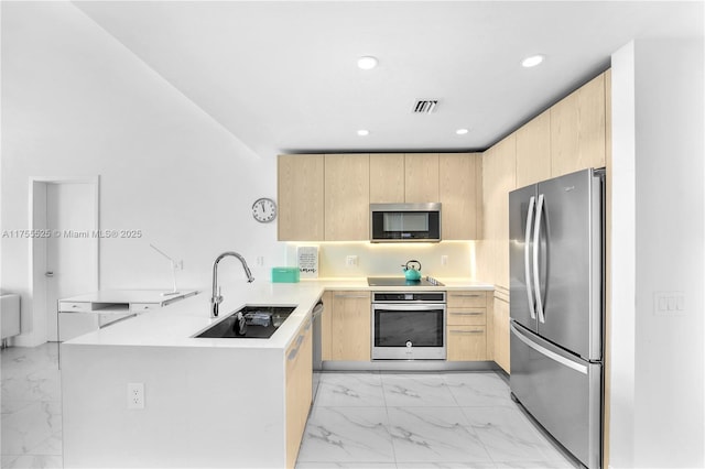 kitchen featuring appliances with stainless steel finishes, light brown cabinets, a sink, and a peninsula