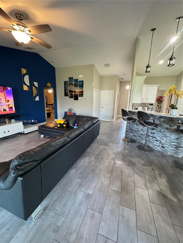 living area featuring lofted ceiling, wood finish floors, visible vents, and a ceiling fan