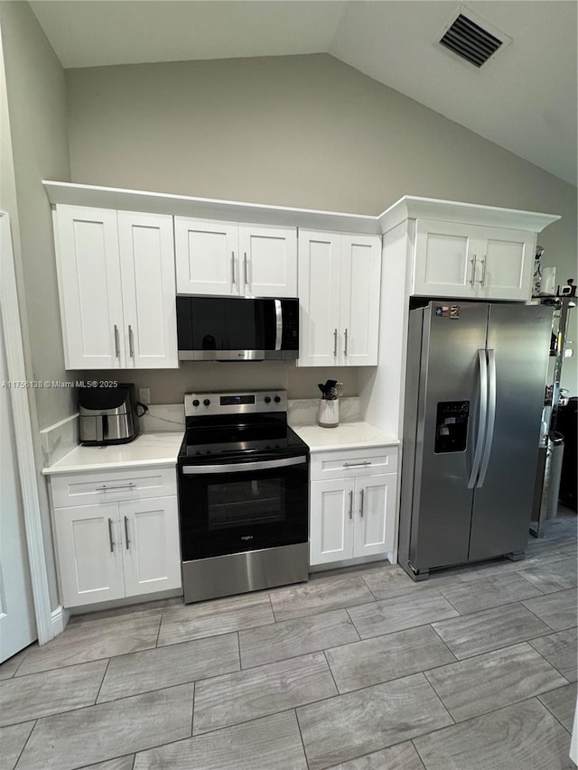 kitchen with visible vents, lofted ceiling, appliances with stainless steel finishes, light countertops, and white cabinetry