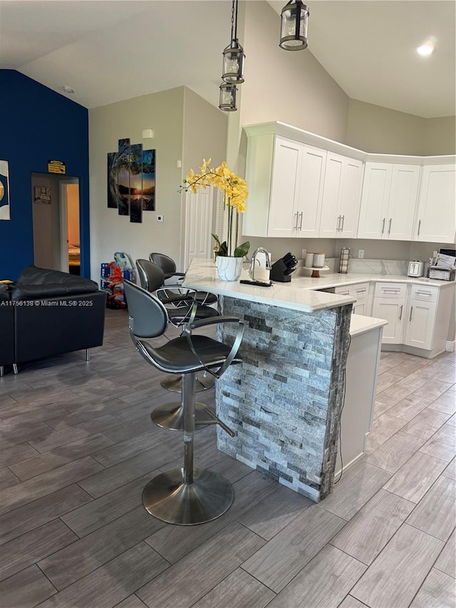 kitchen with a breakfast bar, a peninsula, wood tiled floor, light countertops, and white cabinetry