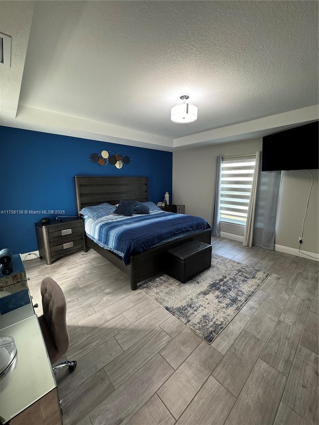 bedroom with baseboards, a textured ceiling, and wood finish floors