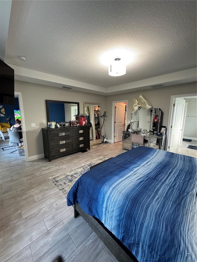 bedroom with a textured ceiling, light wood finished floors, and baseboards