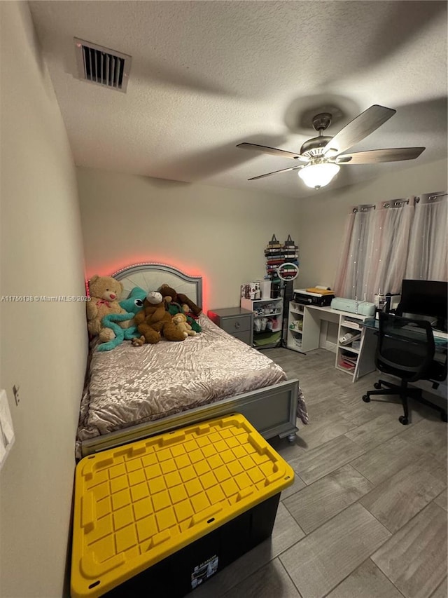 bedroom with a ceiling fan, visible vents, a textured ceiling, and wood finished floors