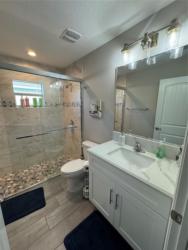 full bathroom featuring visible vents, toilet, a stall shower, wood tiled floor, and vanity