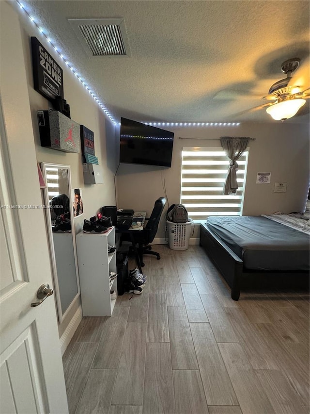 bedroom featuring wood finish floors, visible vents, ceiling fan, and a textured ceiling