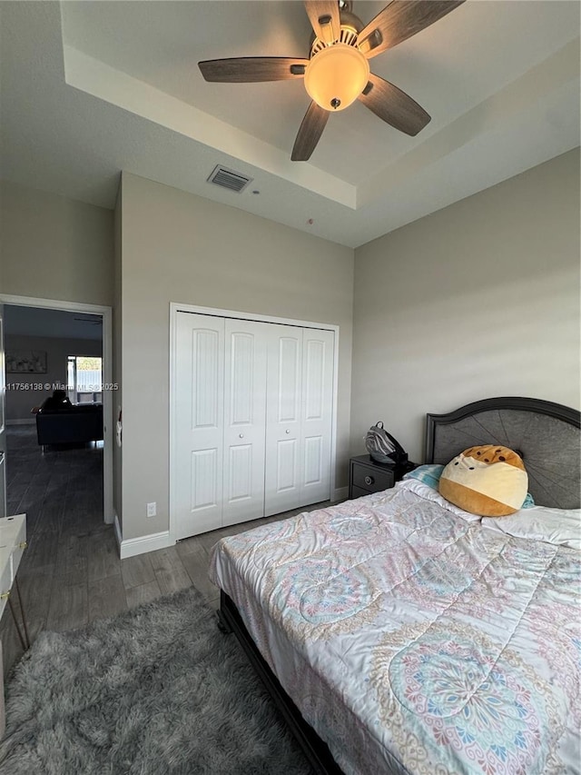 bedroom featuring visible vents, baseboards, a closet, a tray ceiling, and dark wood finished floors