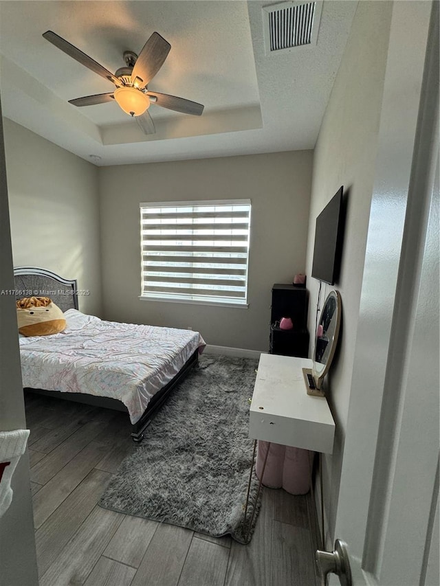 bedroom with visible vents, a tray ceiling, and wood finished floors