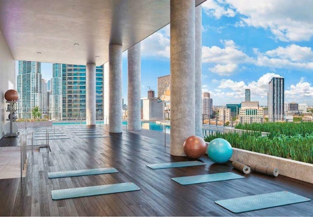 exercise room with a city view, a wall of windows, decorative columns, and wood finished floors