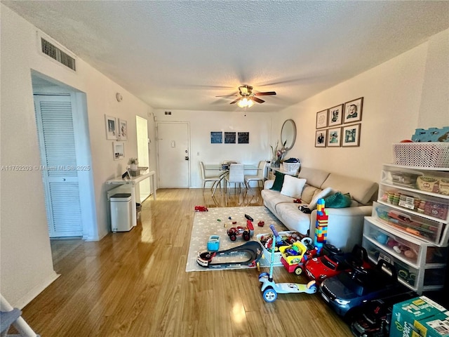 living room with a textured ceiling, wood finished floors, visible vents, and a ceiling fan