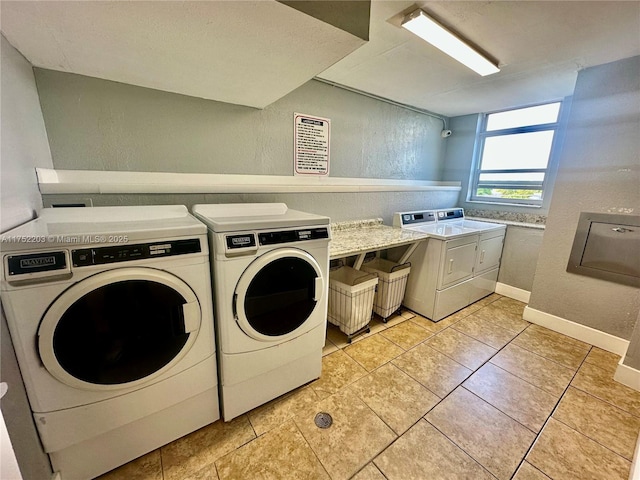 common laundry area featuring washing machine and dryer, a textured wall, baseboards, and light tile patterned floors