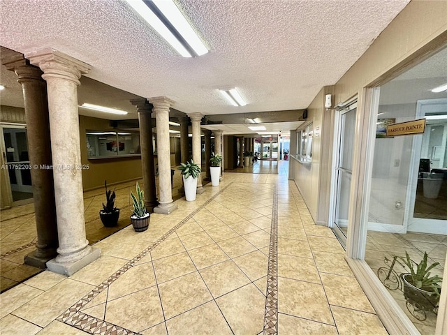 corridor featuring decorative columns, a textured ceiling, baseboards, and tile patterned floors