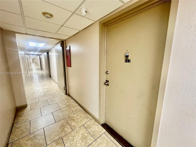 hallway featuring a paneled ceiling, light tile patterned floors, and baseboards