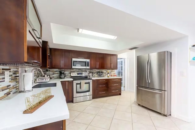 kitchen featuring a tray ceiling, appliances with stainless steel finishes, light countertops, and a sink