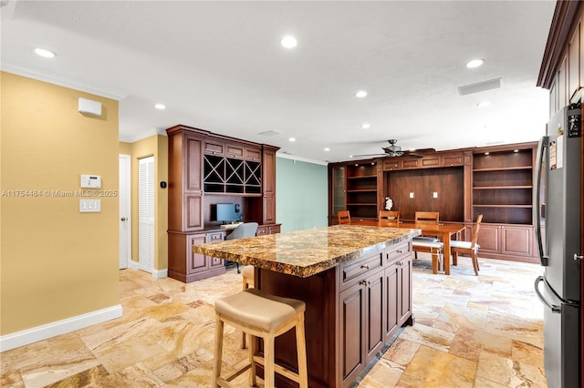 kitchen featuring stone tile floors, recessed lighting, baseboards, freestanding refrigerator, and crown molding