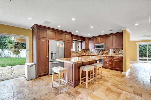 kitchen with a center island, stone tile floors, a breakfast bar area, decorative backsplash, and appliances with stainless steel finishes