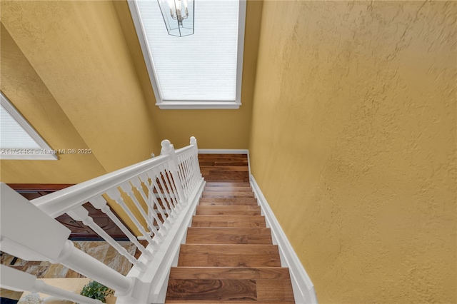 stairs with a chandelier, a textured wall, wood finished floors, and baseboards