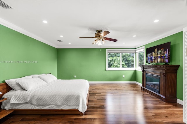 bedroom featuring visible vents, ornamental molding, a glass covered fireplace, wood finished floors, and baseboards