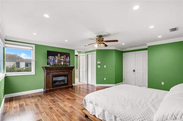 bedroom featuring a glass covered fireplace, wood finished floors, baseboards, and two closets