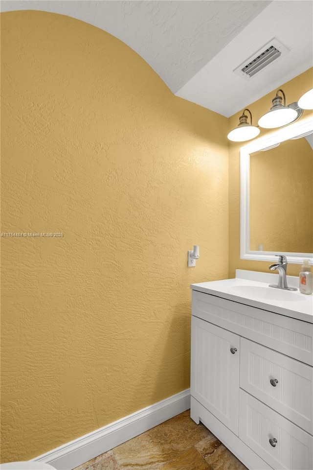 bathroom with visible vents, a textured wall, vanity, and baseboards