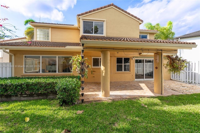 rear view of house featuring a patio, stucco siding, a lawn, fence, and a tiled roof