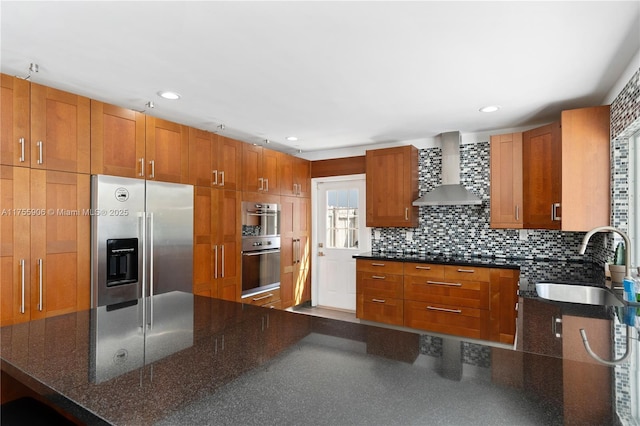 kitchen with wall chimney range hood, decorative backsplash, stainless steel appliances, and a sink