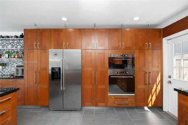 kitchen featuring tasteful backsplash, brown cabinetry, tile patterned floors, multiple ovens, and stainless steel refrigerator with ice dispenser