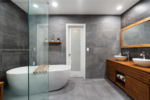 full bath featuring double vanity, a soaking tub, a sink, and tile walls