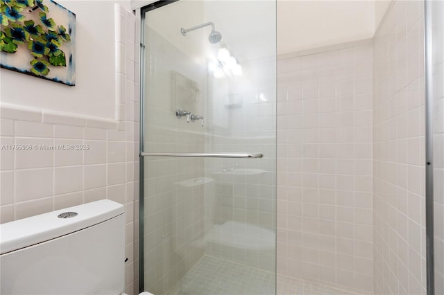 bathroom with wainscoting, tiled shower, tile walls, and toilet