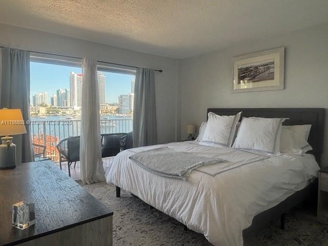 bedroom with access to outside, a city view, and a textured ceiling