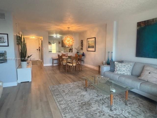 living area featuring baseboards, a textured ceiling, an inviting chandelier, and wood finished floors