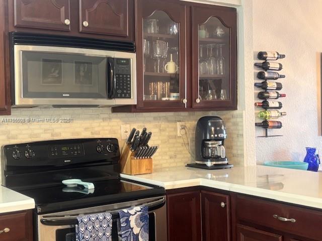 kitchen with glass insert cabinets, stainless steel microwave, range with electric stovetop, and light countertops