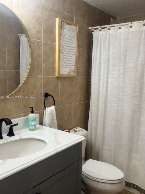 full bathroom featuring a textured ceiling, tile walls, vanity, and toilet