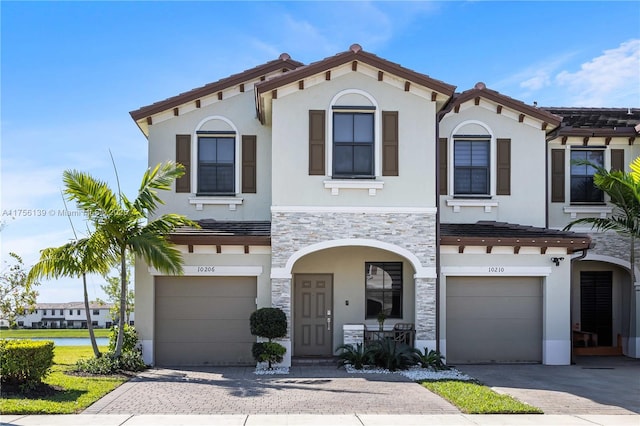 mediterranean / spanish-style home featuring stone siding, decorative driveway, and an attached garage