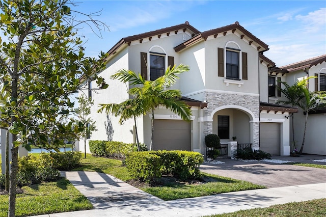 mediterranean / spanish house with a garage, stone siding, decorative driveway, and stucco siding