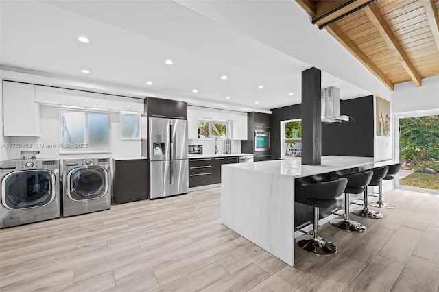 kitchen featuring modern cabinets, a kitchen breakfast bar, stainless steel appliances, washer and dryer, and beam ceiling